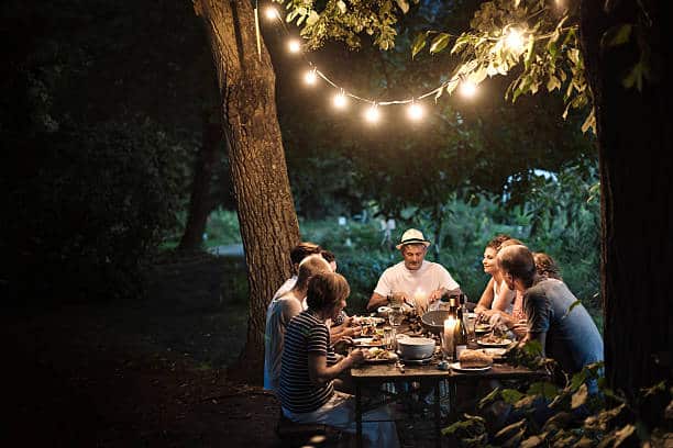 Famille qui dîne dans le salon de jardin, éclairée par une guirlande lumineuse accrochée à un arbre